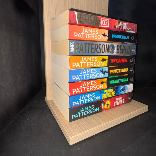 Row of books by James Patterson on a wooden shelf against a dark background