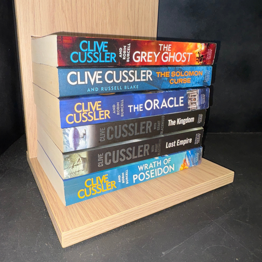 Stack of Clive Cussler books on a wooden stand against a black background