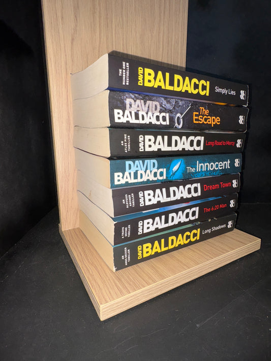 Row of books by David Baldacci on a wooden shelf against a dark background